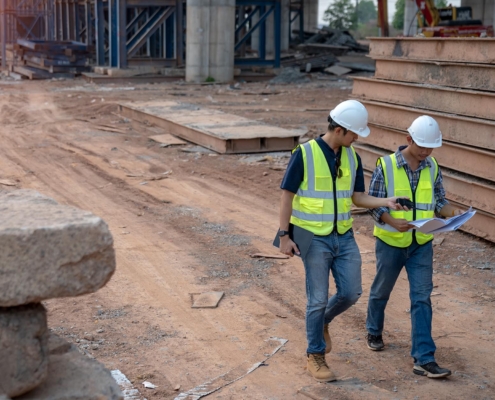 Side view of two construction workers looking over plans while walking through construction site