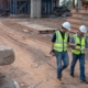 Side view of two construction workers looking over plans while walking through construction site